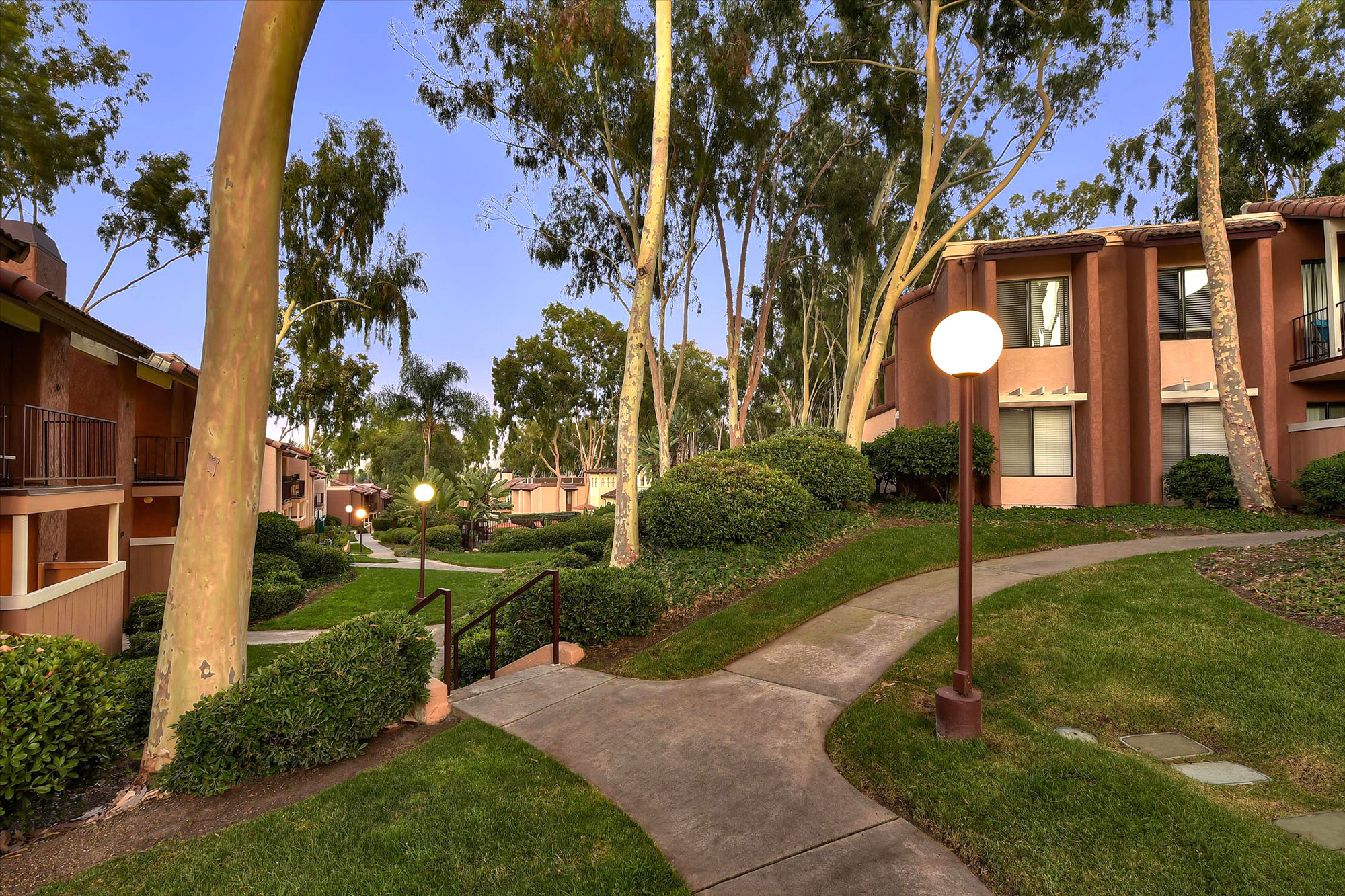Exterior dusk shot of outside apartment complex, garden landscaping, and walking path