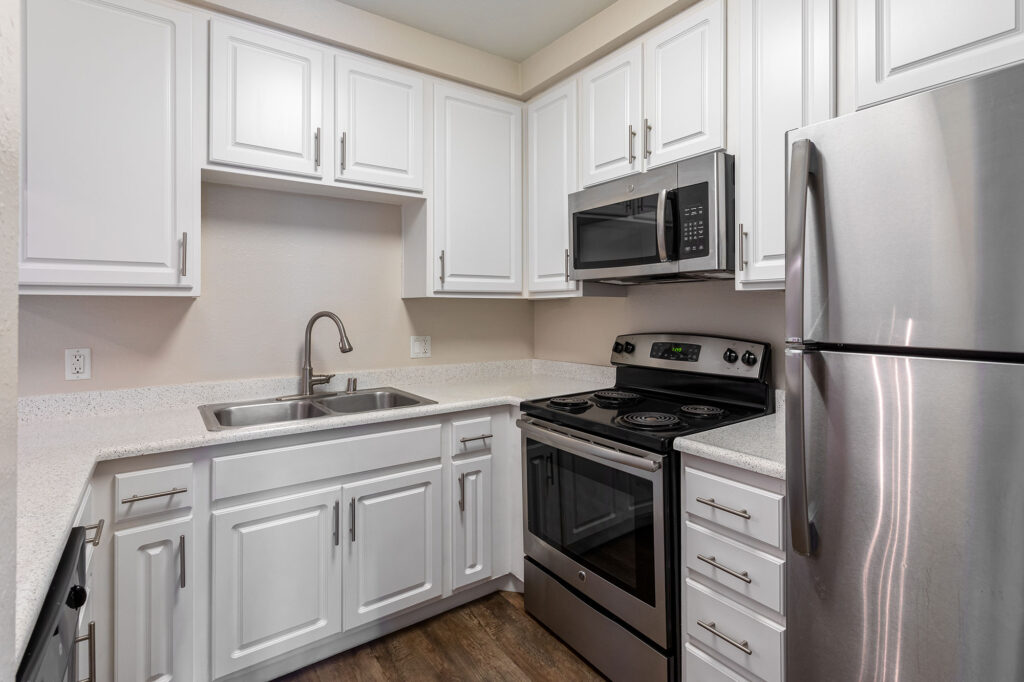 Interior shot of kitchen with wood-style flooring, designer lighting, stainless steel appliances and dual sink