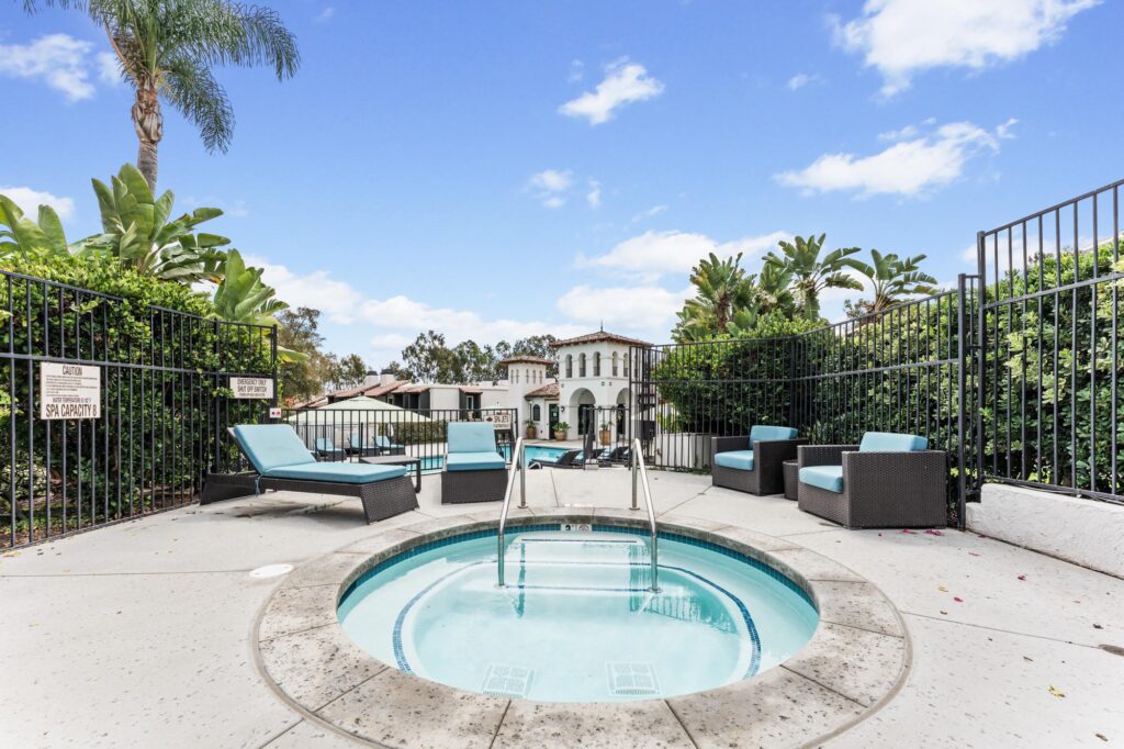 Hot tub surrounded by lounge chairs, lush greenery and apartments on a pool deck.