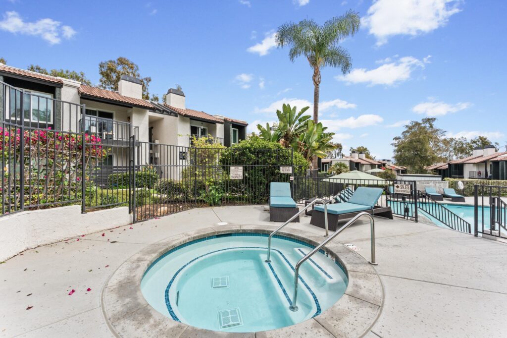 Hot tub surrounded by lounge chairs, lush greenery and apartments on a pool deck.